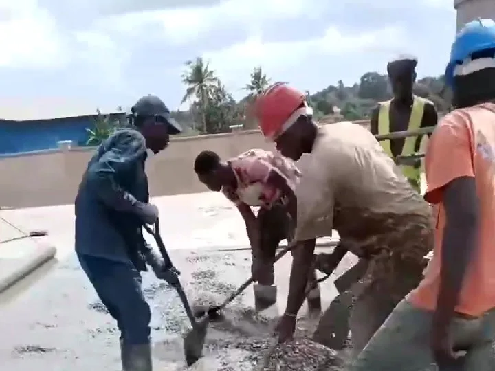 Five workers spreading fresh concrete across a slab with shovels, palm trees on the horizon