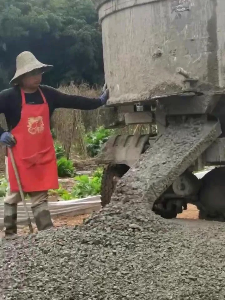 Close view of concrete falling from the discharge chute of a self-loading mixer while a worker steadies the drum