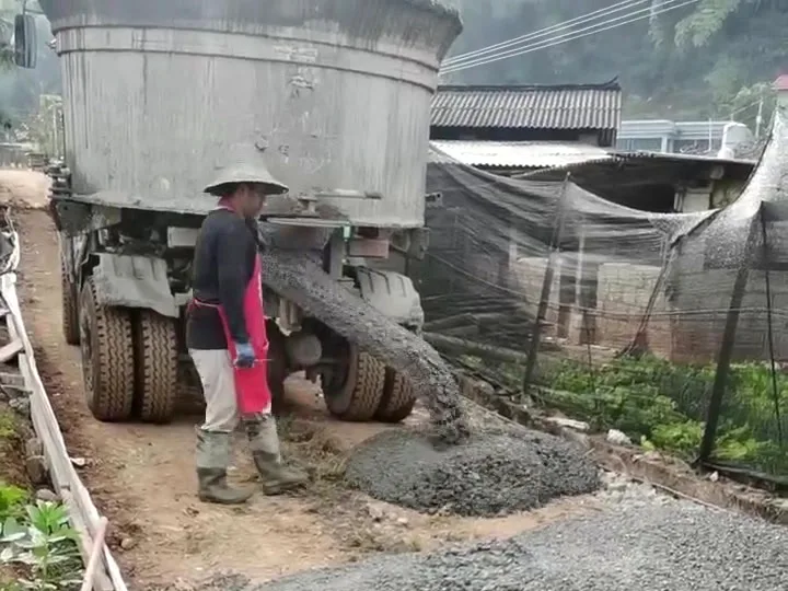 Self-loading mixer discharging concrete through its chute onto a village road under construction